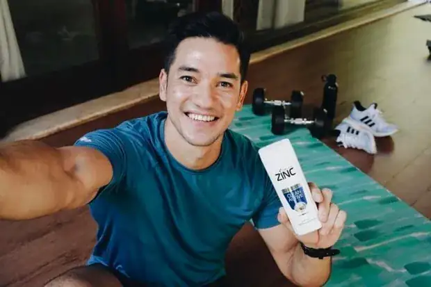 A creator taking a selfie on a yoga mat at home, holding up a bottle of ZINC Clean & Active shampoo
