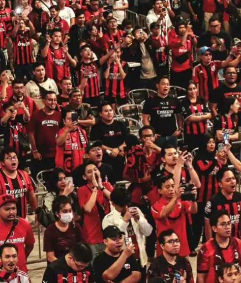 A crowd of AC Milan supporters in club shirts cheering and filming at a BMI community event