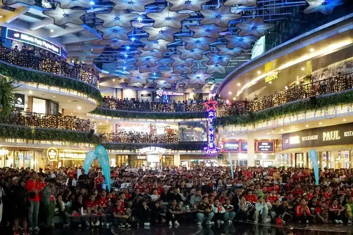 A packed mall atrium of fans in red shirts watching a live match screening run by MIX, under a canopy of lit star lanterns