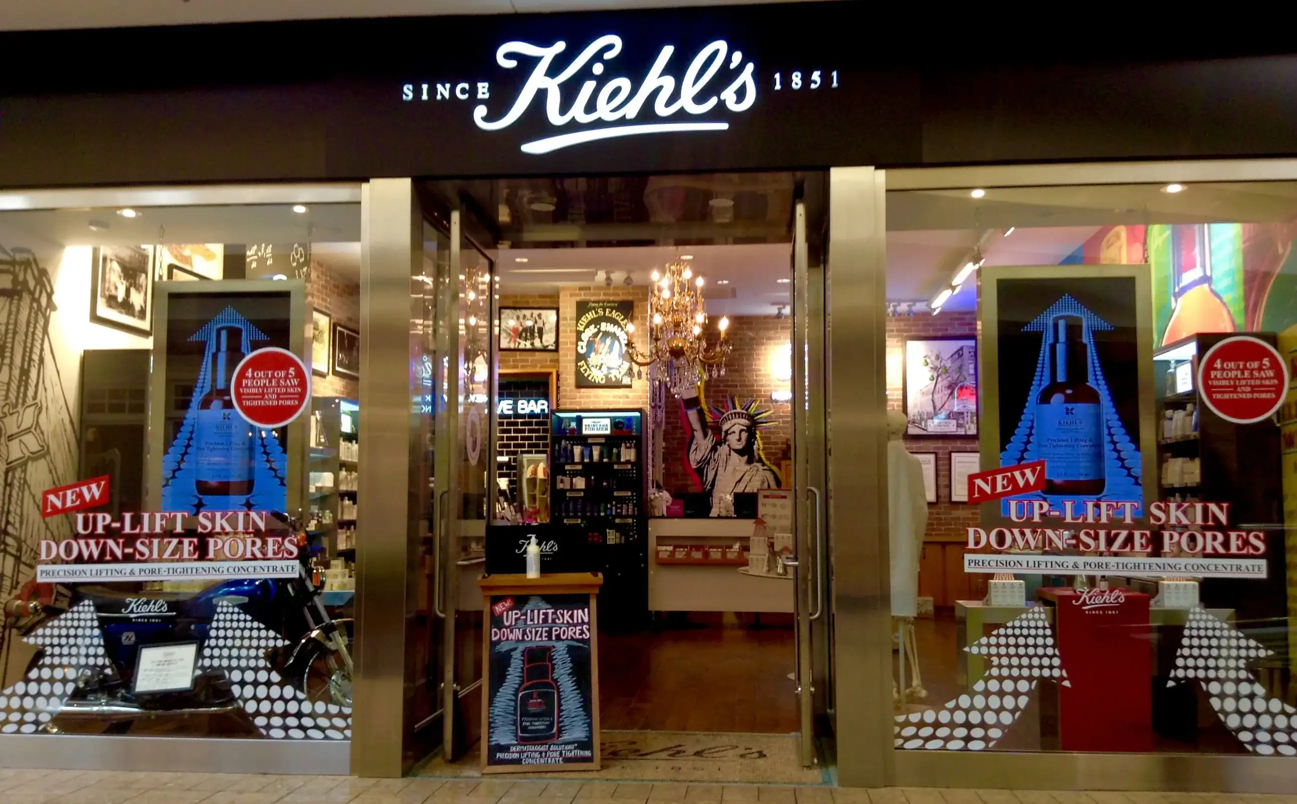 A Kiehl's store front at night, its lit logo above glass doors and window displays
