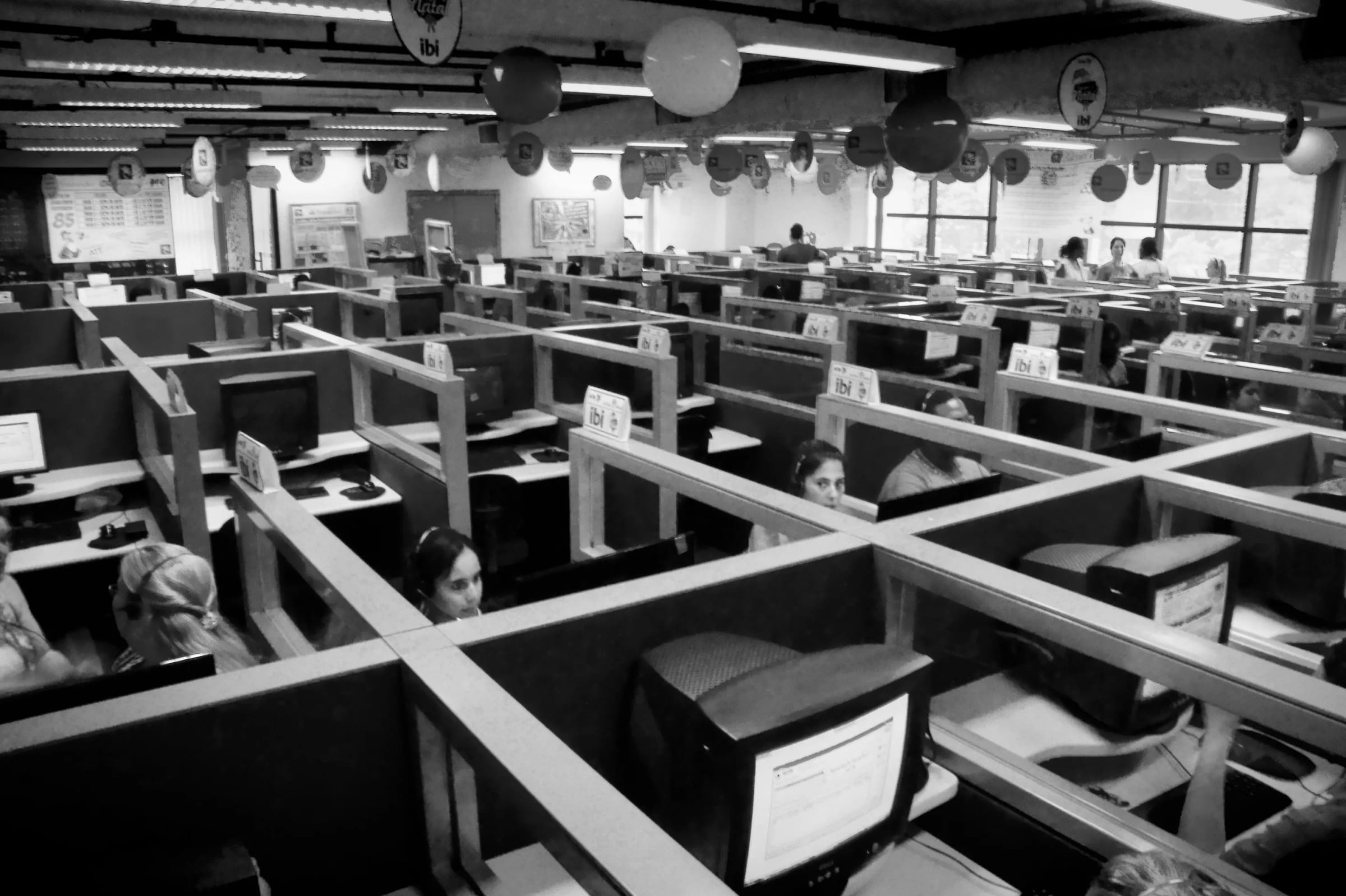 Rows of call center cubicles, with agents in headsets working at computer screens, in black and white