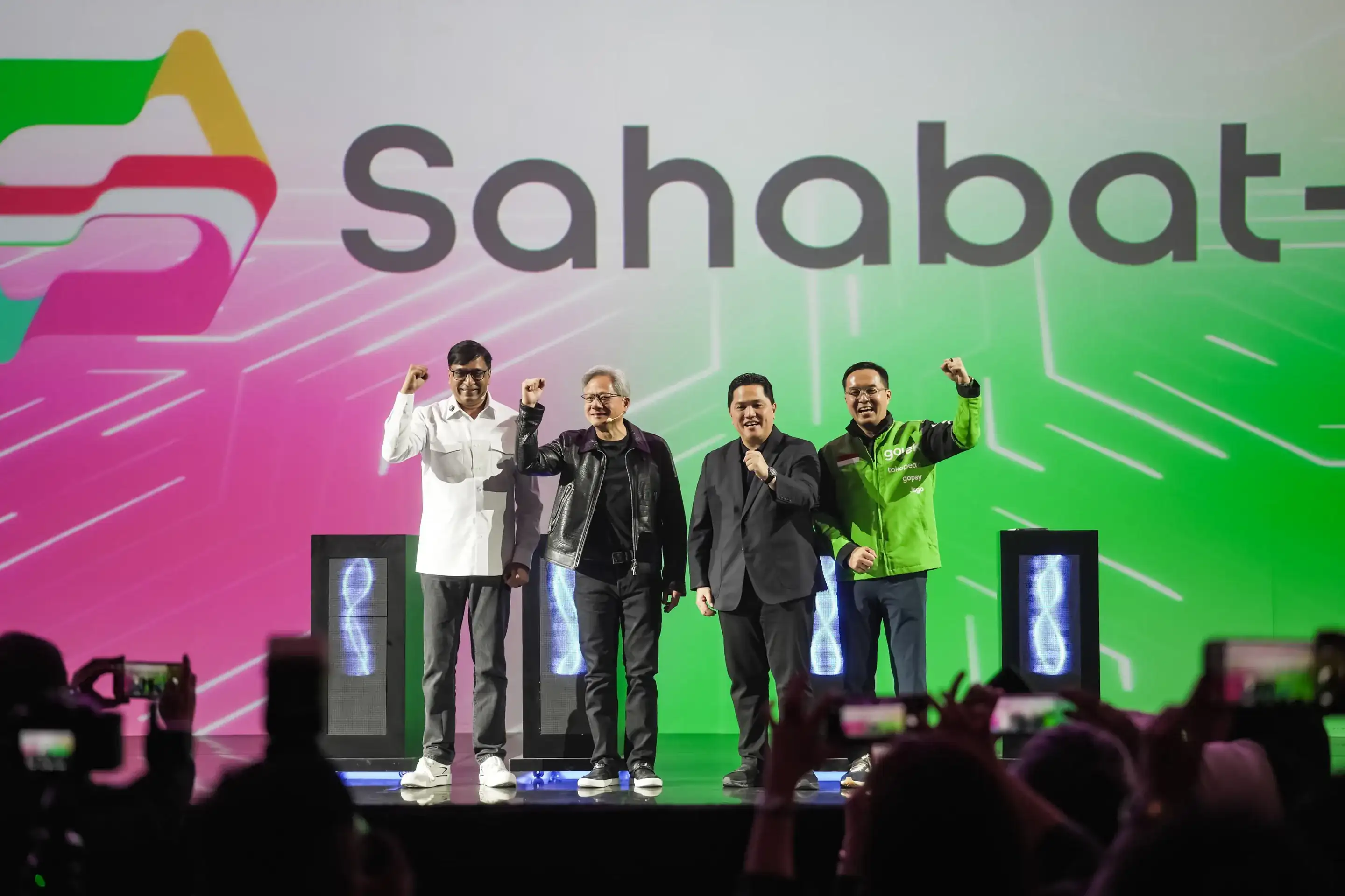 Four people on a stage raising their fists in front of a large Sahabat-AI sign