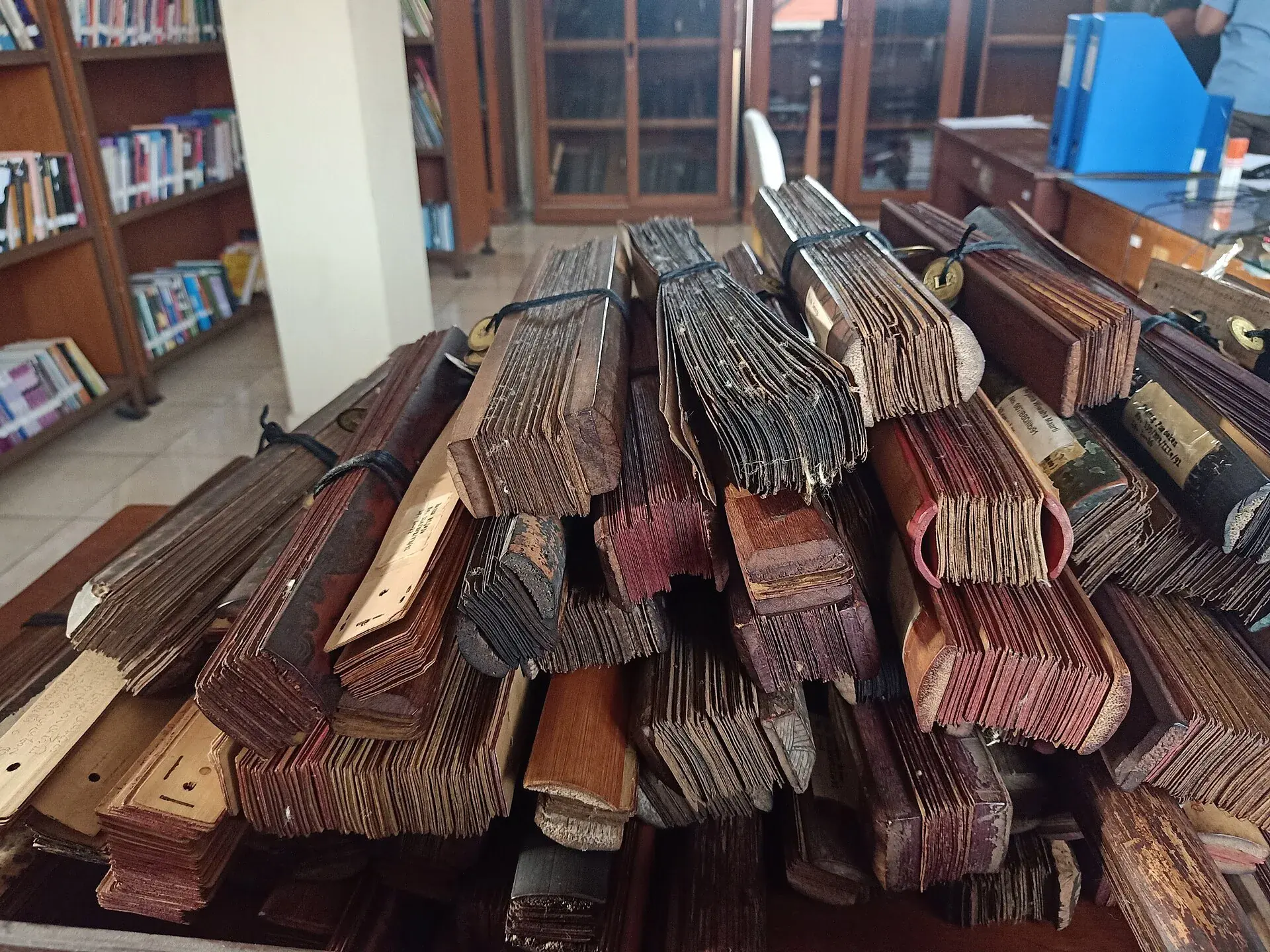 A stack of bound palm-leaf lontar manuscripts on a library table