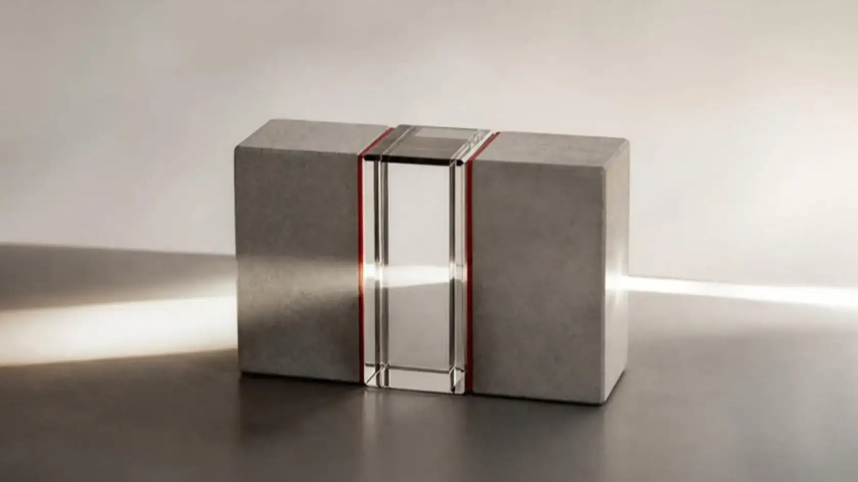 A concrete block split by a clear glass core edged in red, a beam of light passing straight through it