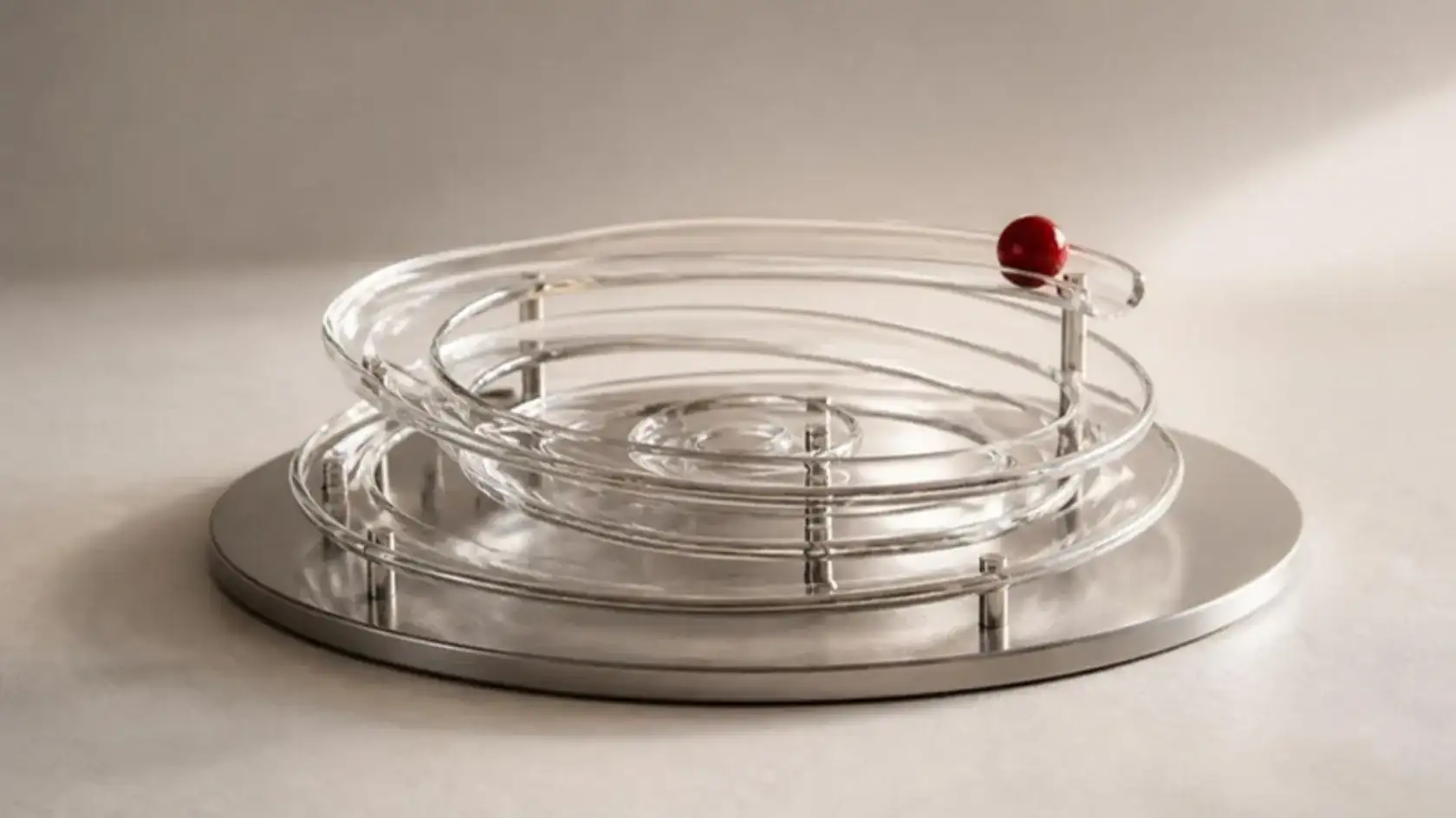 Glass rings rising in a widening spiral from a steel plate, a red bead traveling along the top