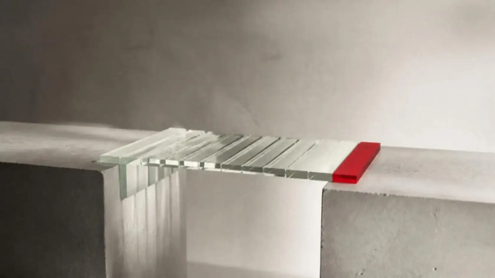 Clear glass panes bridging the gap between two concrete blocks, the last pane red