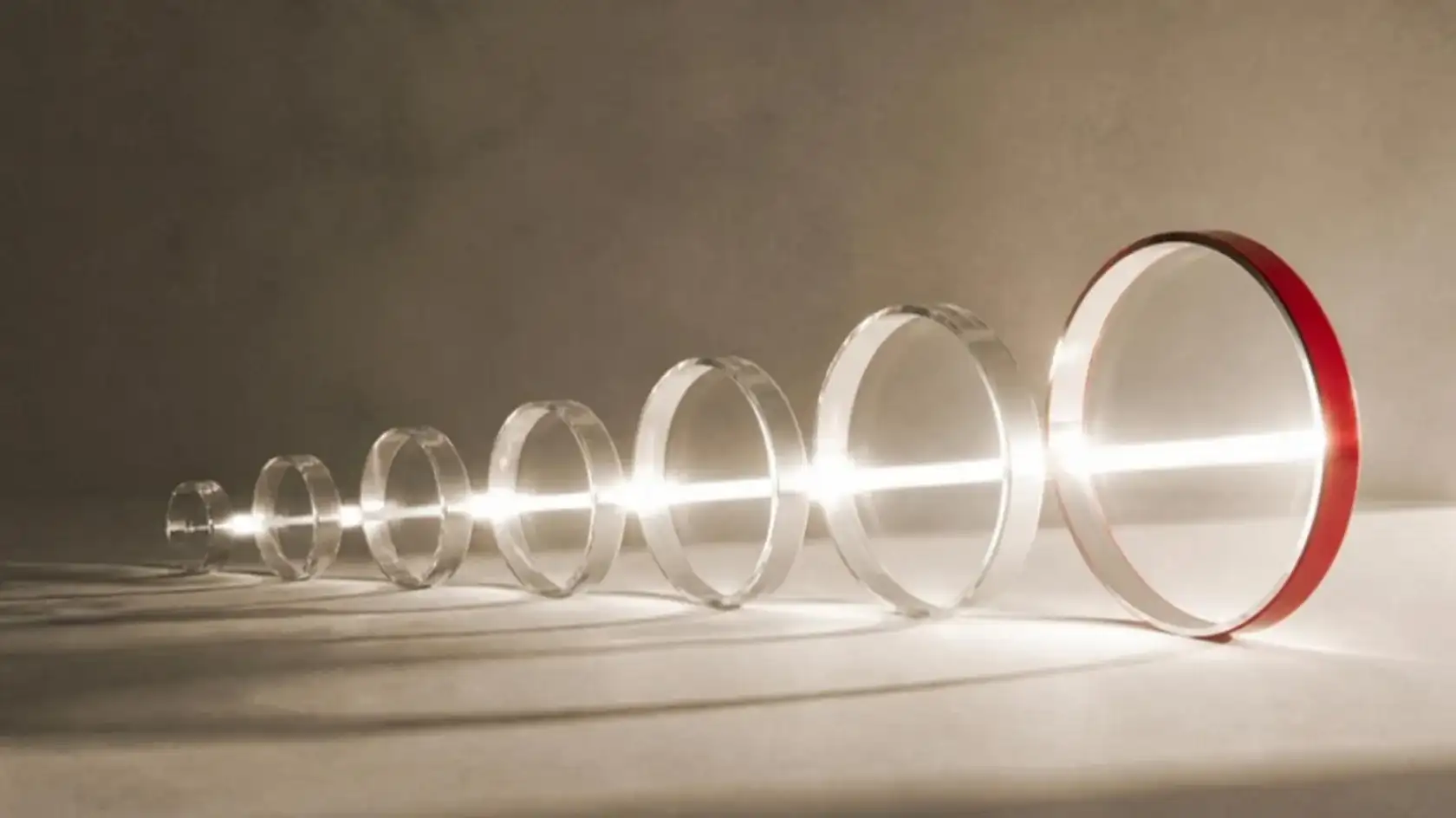 A line of glass rings growing in size along a beam of light, the largest rimmed in red