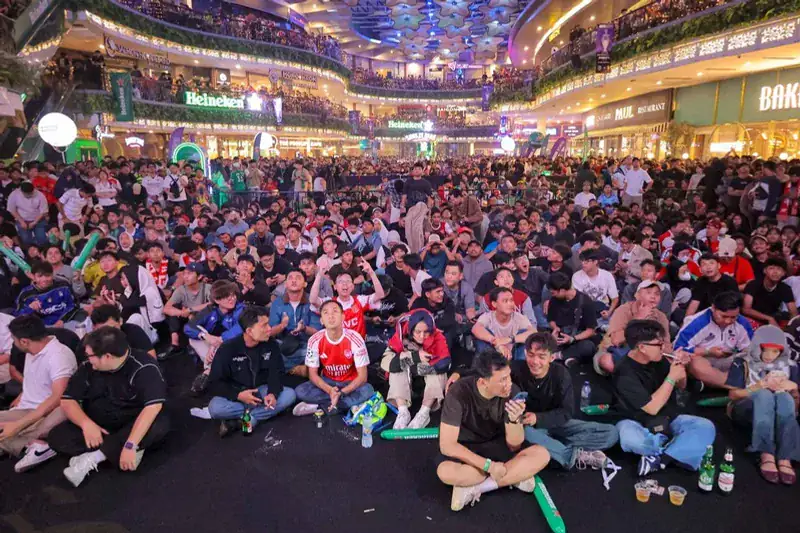 A packed mall atrium of football fans watching the final on a big screen, Heineken branding on the balconies above